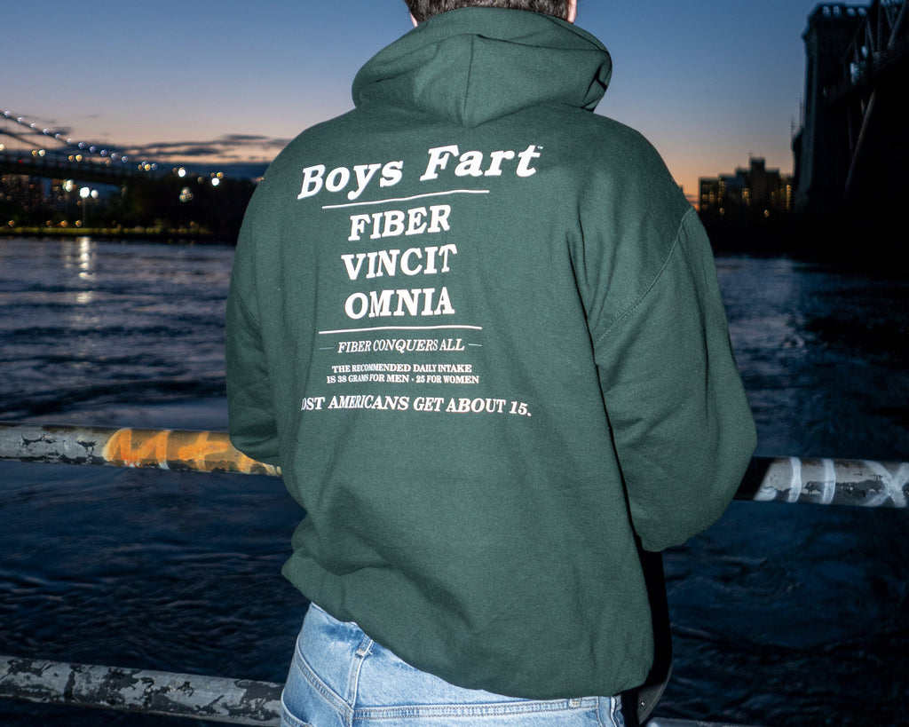 Person wearing a green jacket with text standing by a waterfront at dusk.
